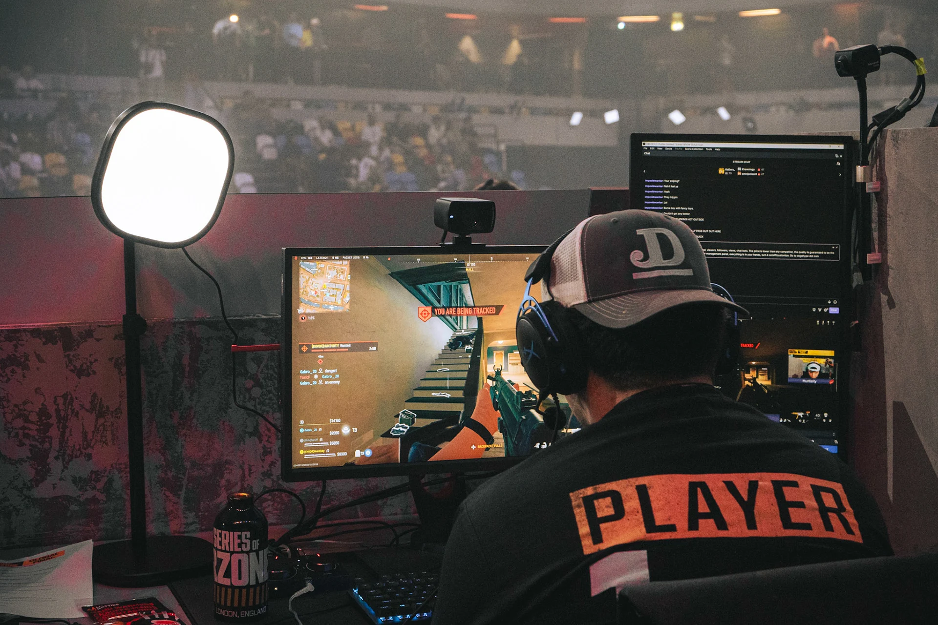 A man sitting behind a computer playing call of duty in an event with lots people in the crowd. Photo taken by Troy the shooter.